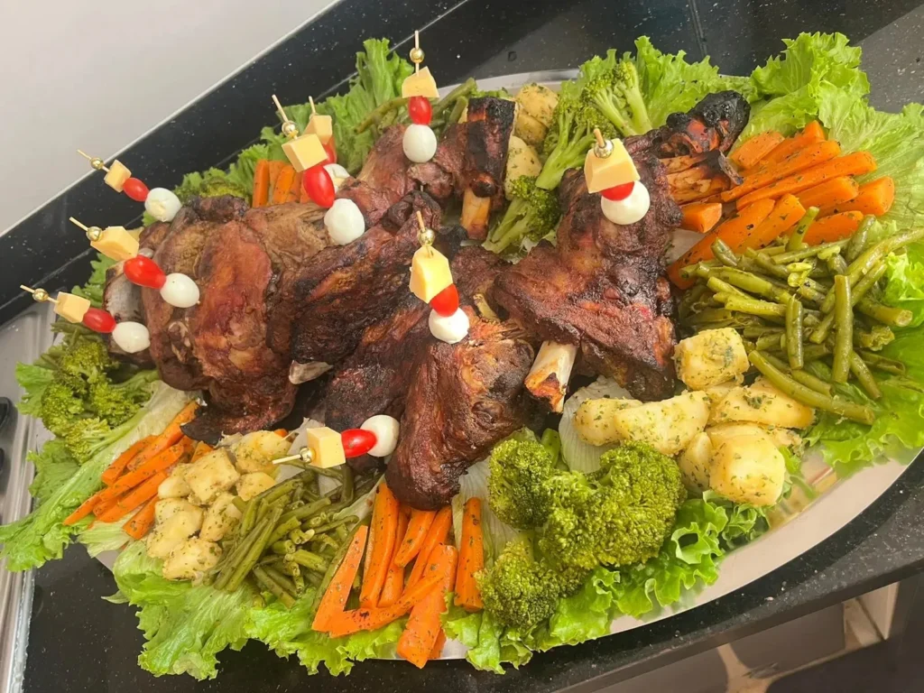 A beautifully arranged platter of grilled lamb with roasted vegetables, fresh lettuce, and cheese-tomato skewers.