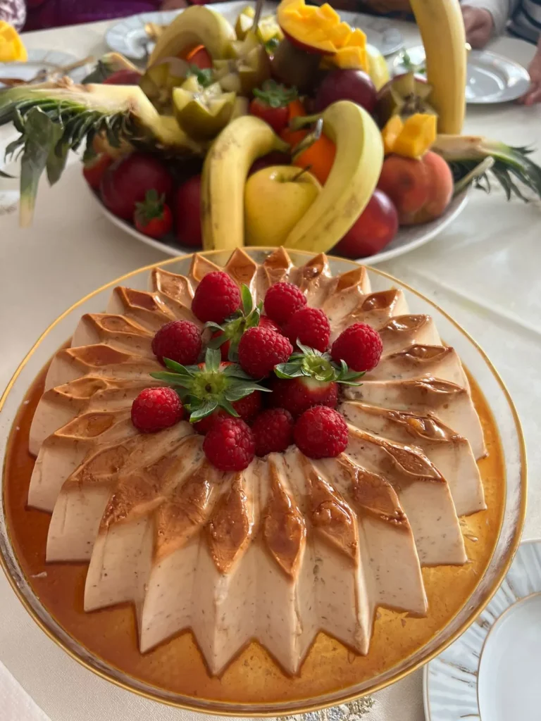 Elegant caramel flan dessert topped with fresh raspberries, served alongside a vibrant fruit platter.