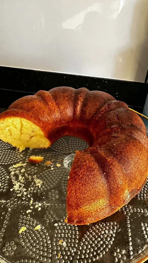 Freshly baked golden brown bundt cake with a moist texture, partially sliced on a glass plate.